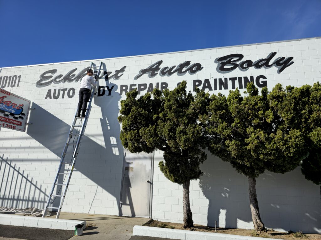auto body shop in the process of being painted with white for the walls and stenciling the business lettering