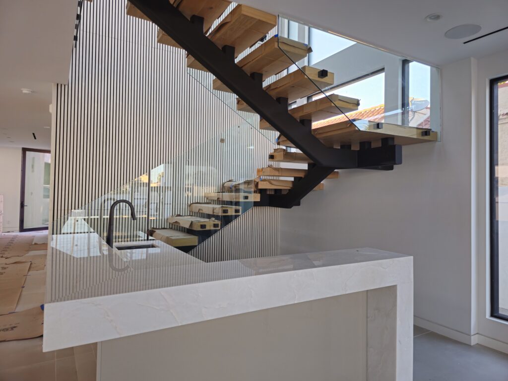 Modern high-end and minimalist interior of a beverly hills home with modern and fresh staircase with glass railing and wood steps. White walls with ample natural lighting.